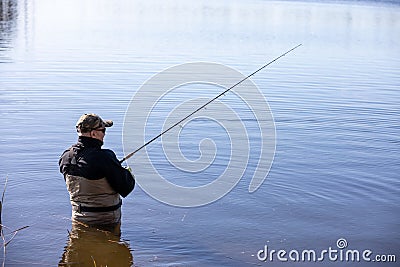 Fisherman in waders catches pike in the lake Stock Photo