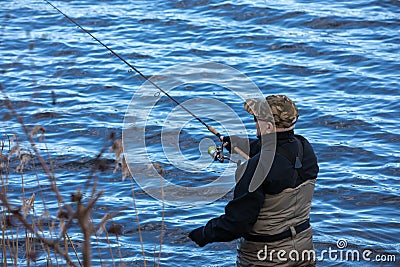 Fisherman in waders catches pike in the lake Stock Photo