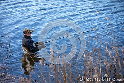 Fisherman in waders catches pike in the lake Stock Photo