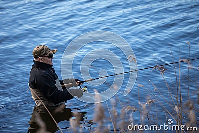 Fisherman in waders catches pike in the lake Stock Photo