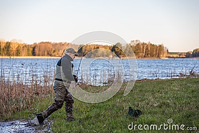 Fisherman in waders comes out of the river to the river bank Stock Photo