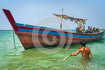 A fisherman wades out in waist deep water to his colourful wooden boat off the beach at Ngapali, Myanmar Editorial Stock Photo