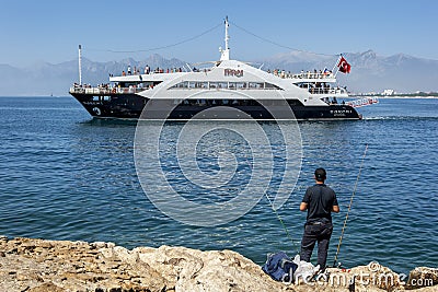 A fisherman watches a cruise ship move through Antalya Bay in Turkey. Editorial Stock Photo