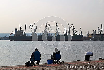 Fishermen fishing with a rod at the pier in the seaport on a warm windless autumn day Editorial Stock Photo