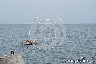 Fishermen with rods dressed in protective vests sitting with backs to viewer in black rubber boat on background of sea horizon Editorial Stock Photo