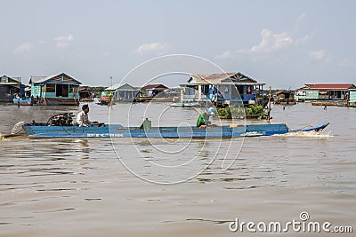 Cambodia, Tonle Sap Lake, February 2012: Fishermen sail on a boat against the backdrop of huts on the water. Life of the Editorial Stock Photo