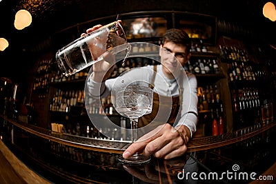 Fisheye shot attractive male bartender pouring a cocktail from the measuring cup to the glass Stock Photo