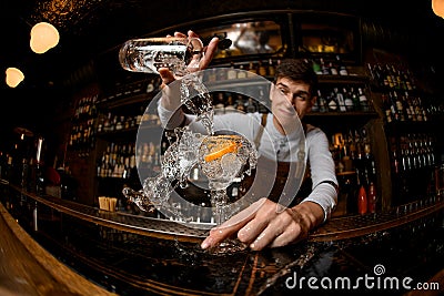 Fisheye shot male bartender pouring a cocktail from the measuring cup to the glass with orange zest Stock Photo