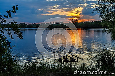 Fishing adventures, carp fishing. Angler, at sunset, is fishing with carpfishing technique. Camping on the shore of the lake.Carp Stock Photo