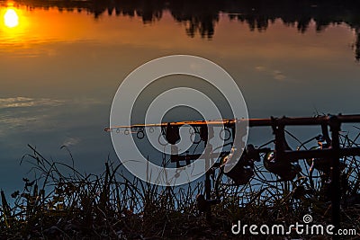 Fishing adventures, carp fishing. Angler, at sunset, is fishing with carpfishing technique. Camping on the shore of the lake.Carp Stock Photo