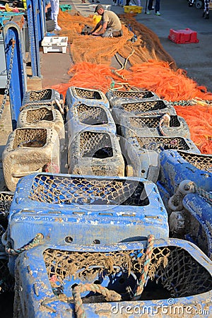 WHITSTABLE, UK - OCTOBER 15, 2017: Fishing boxes and colorful fishing nets with a fisherman working on his nets in the background Editorial Stock Photo