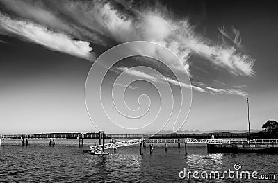 A fishing pier with strong horizontal lines contrasts against a summer sky marked by fluffy diagonal aligned clouds Stock Photo