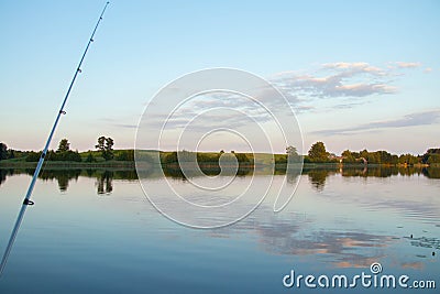 fishing rod against bright lake with reeds forest and bridge at sunny summer day Stock Photo