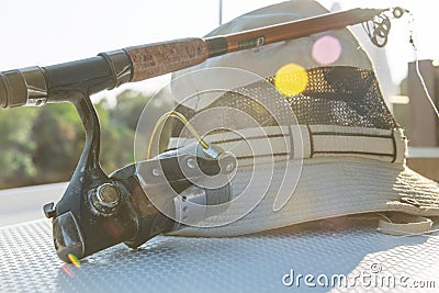 Fishing rod and hat prepared to go fishind in summer day with blinks of sun Stock Photo