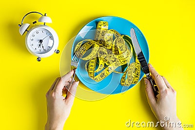 fist on a plate with a measuring tape. Alarm clock. Woman hands hold fork and knife Stock Photo