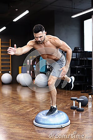 Fit athlete performing exercise on gymnastic hemisphere bosu ball in gym Stock Photo