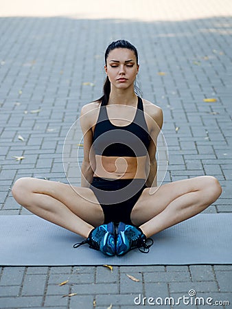 A fit, athlete young woman sitting down on the mat, doing stretching exercises outside. Healthy lifestyle Stock Photo