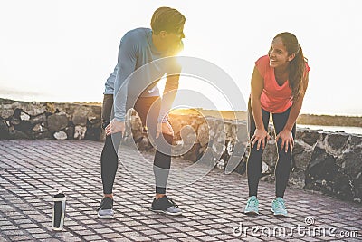 Fit couple taking a rest after fast running workout - Joggers training outdoor at sunset together - Main focus on girl face - Stock Photo