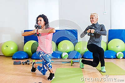 Fit female sportswoman doing curtsy lunge exercise with dumbbells in group fitness studio class Stock Photo