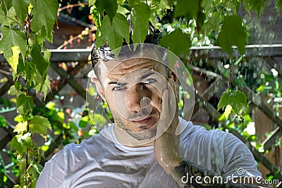 Handsome semi naked man with muscles and bare chest caught in shower of rain in garden Stock Photo