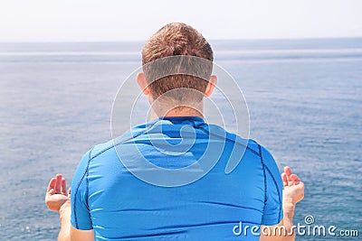 A fit man in the Lotus position on a seashore. Young fitness man doing yoga outdoors. Stock Photo