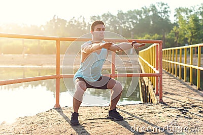 Fit man warming up doing squats stretching arms forward outdoors. Stock Photo