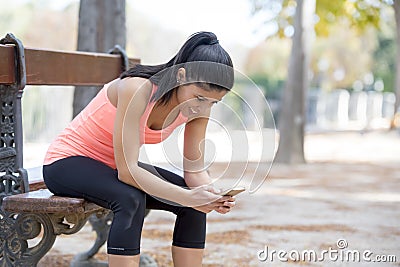 Fit sport woman looking at mobile phone internet app tracking performance after running workout sitting on park bench happy Stock Photo