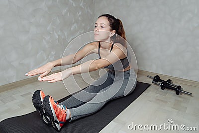 Fit woman stretching her leg to warm up on grey mat at home. Fitness concept, close up on sport shoes Stock Photo