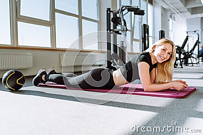 Fit young female lying on exercise mat in gym and adorably smiling. Healthy woman take break after workout. Stock Photo