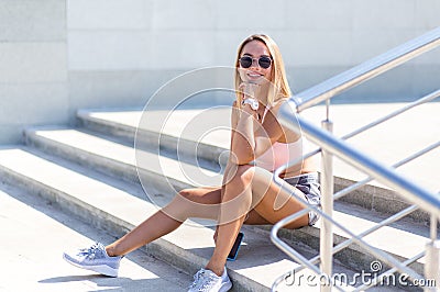 Fit young girl with blond hair in a sports top and shorts sits on the stairs and smiles Stock Photo