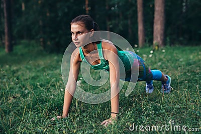 Fit young woman doing push-up exercise on grass in forest Stock Photo