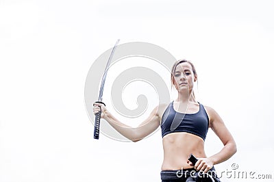 Fit young woman in sports bra holding katana in hawk wing position and looking at camera Stock Photo