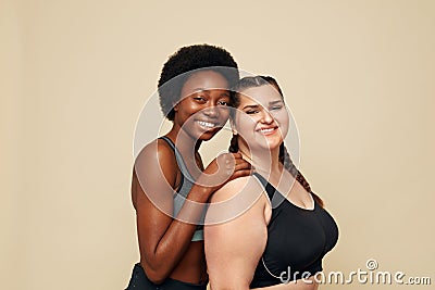 Fitness. Different Ethnicity Women Portrait. Caucasian And African Models In Fitness Clothes Posing On Beige Background. Stock Photo