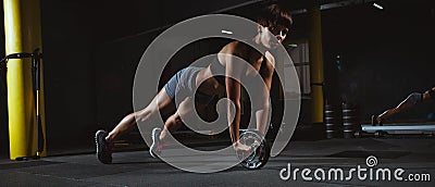 Fitness girl doing crossfit exercises in gym with wheel in dark Stock Photo