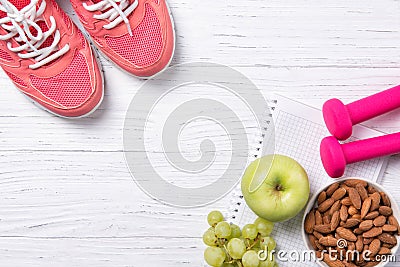 Fitness and healthy eating concept, pink sneakers and dumbbells with apple, grapes and almond nuts on notepad, wooden background Stock Photo