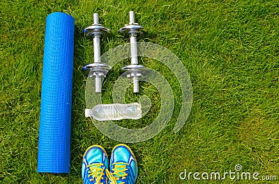 Fitness and healthy lifestyle concept, sport shoes, dumbbells, bottle of water and mat on grass Stock Photo