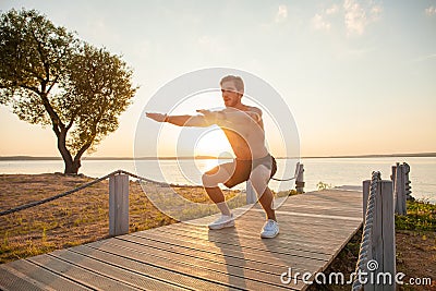 Fitness man training air squat exercise on beach outside. Fit male exercising crossfit outside. Young handsome caucasian Stock Photo