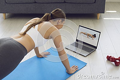 Fitness online. Young fit girl at home on the floor doing exercises, stretching warm-up and uses a video fitness lesson Stock Photo