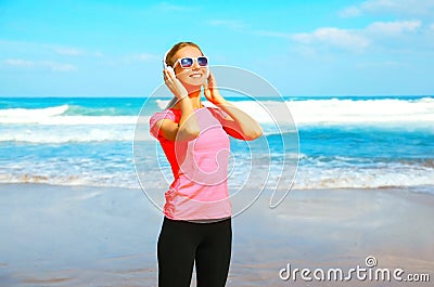 Fitness smiling woman listens to music in wireless headphones on the beach Stock Photo