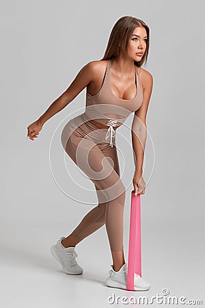 Fitness woman doing exercise for glutes with resistance band on gray background. Athletic girl working out Stock Photo