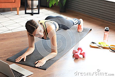 Fitness woman doing plank and watching online tutorials on laptop, training in living room. Stay at home activities Stock Photo