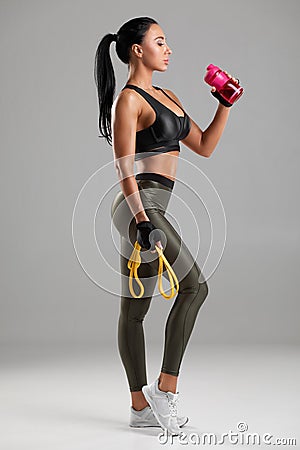 Fitness woman drinking water from a bottle, isolated on gray background. Active girl quenches thirst Stock Photo