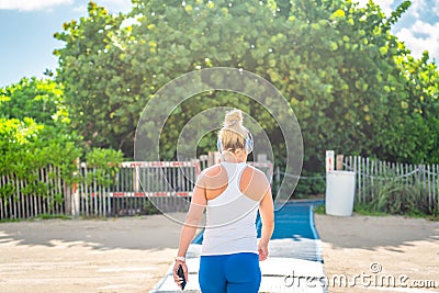 Fitness woman listening to music in sportswear with wireless in-ear headphones on summer ocean beach in Miami Editorial Stock Photo