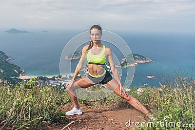 Fitness woman stretching her leg muscles doing side lunge exercise preparing for cardio work-out in mountains by the sea Stock Photo