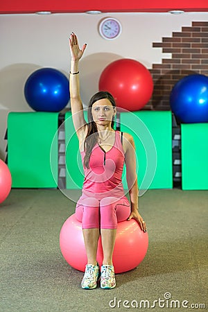 Fitness. Young beautiful white girl in a pink sports suit does physical exercises with a pink fit ball at the fitness center. Stock Photo