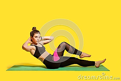 Fitness young woman with hair bun in tight sportswear training on gym mat, doing sit ups crunch, exercising Stock Photo