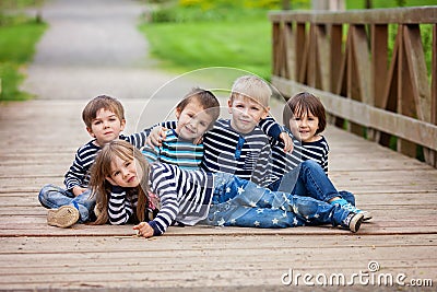 Five adorable kids, dressed in striped shirts, sitting on a bridge in the park Stock Photo