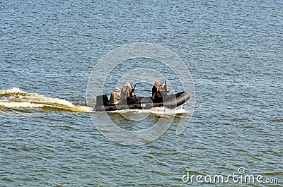 Five military men with weapons and special equipment in the black motor boat. Special operations forces Stock Photo