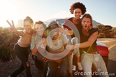 Five millennial friends on a road trip have fun posing for photos at the roadside, lens flare Stock Photo