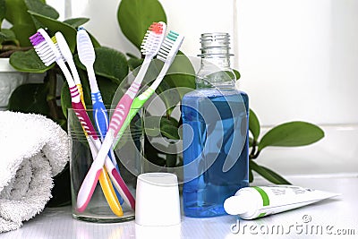 Five toothbrushes in a glass cup mouthwash a tube of toothpaste and a rolled up towel on the dressing table against a backdrop of Stock Photo